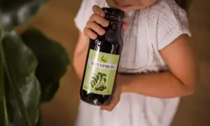 Dziecko trzyma butelkę syropu z czarnego bzu, który jest naturalnym wsparciem dla odporności.