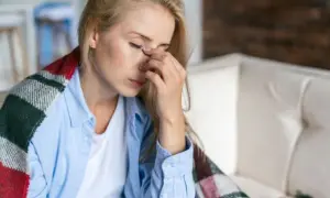 Kobieta z zasłoniętymi oczami, trzymająca się za nos, otulona kocem. Zastanawia się, jak długo rozwija się sepsa.