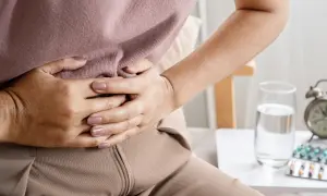 Kobieta trzyma się za brzuch, szukając domowych sposobów na wzdęcia. Obok szklanka wody i leki.