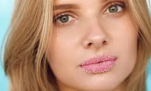 Domowy peeling do ust z cukru nałożony na pełne, różowe usta młodej kobiety.