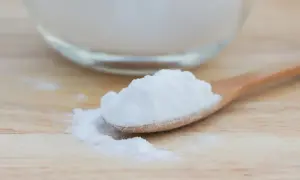 Łyżka z sodą oczyszczoną, która może pomóc na zgagę. W tle szklana miska z proszkiem.
