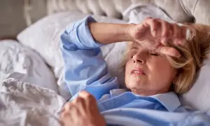 Kobieta w łóżku z ręką na czole, doświadczająca pocenia się w nocy bez gorączki.