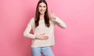Uśmiechnięta kobieta pokazuje kciuk w górę i dotyka brzucha, symbolizując, jak wyleczyłem refluks.
