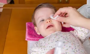 Delikatne przemywanie oczu niemowlaka wacikiem nasączonym solą fizjologiczną do oczu.