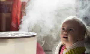 Mała dziewczynka z zaciekawieniem patrzy na parę wydobywającą się z nawilżacza, który pomaga w inhalacjach z soli fizjologicznej.