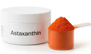 Biały pojemnik z napisem "Astaxanthin" obok miarki z pomarańczowym proszkiem. Czy astaksantyna skutki uboczne są groźne?