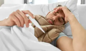 Chory mężczyzna w łóżku z termometrem. Zastanawia się, od jakiej temperatury zbijać gorączkę u dorosłego.