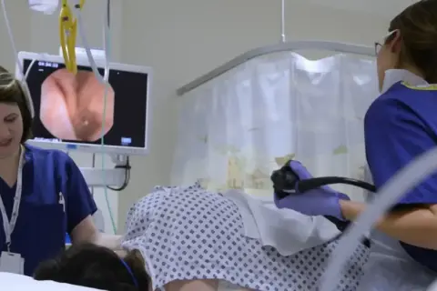 Lekarze przygotowują pacjenta do kolonoskopii, monitorując obraz z endoskopu na ekranie.