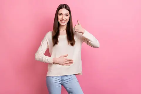 Uśmiechnięta kobieta pokazuje kciuk w górę i dotyka brzucha, symbolizując, jak wyleczyłem refluks.