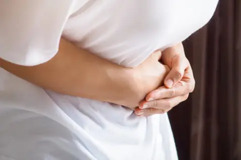 Osoba trzyma się za brzuch, odczuwając ostry ból w lewym boku.