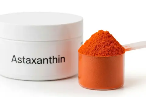Biały pojemnik z napisem "Astaxanthin" obok miarki z pomarańczowym proszkiem. Czy astaksantyna skutki uboczne są groźne?