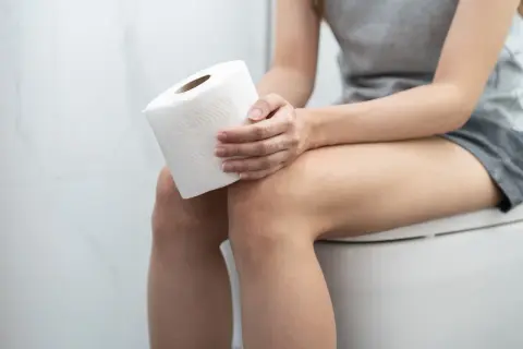 Kobieta siedzi na toalecie z rolką papieru. Czy witamina D3 a zapach moczu mogą być powiązane?