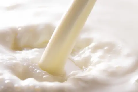 Strumień mleka koziego, znanego z cennych właściwości, tworzy fale i bąbelki w białej, kremowej masie.