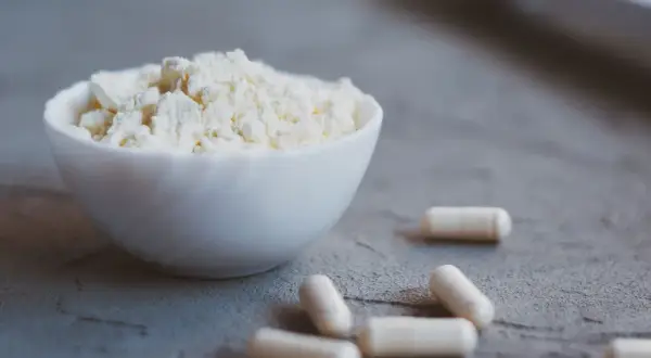 Biały proszek w miseczce i kapsułki. Colostrum na co? Na wsparcie odporności i regeneracji.