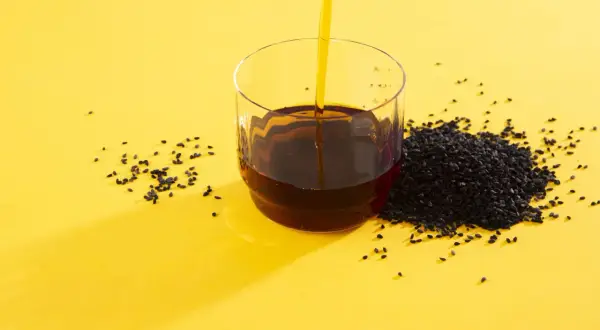 Olej z czarnuszki w szklance, obok nasiona. Zanim zaczniesz stosować, sprawdź olej z czarnuszki przeciwwskazania.