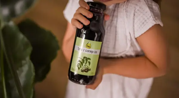 Dziecko trzyma butelkę syropu z czarnego bzu, który jest naturalnym wsparciem dla odporności.
