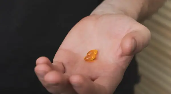 Dwie bursztynowe kapsułki na dłoni, symbolizujące walkę z niedoborem witaminy D3.
