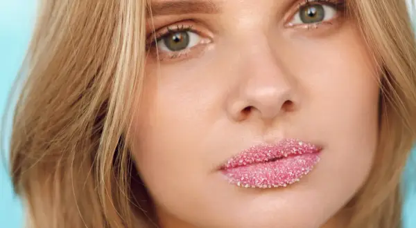 Domowy peeling do ust z cukru nałożony na pełne, różowe usta młodej kobiety.