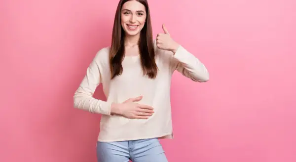 Uśmiechnięta kobieta pokazuje kciuk w górę i dotyka brzucha, symbolizując, jak wyleczyłem refluks.