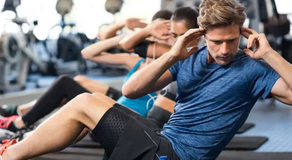 Ludzie ćwiczą brzuszki w siłowni. Regularny trening to sposób, jak obniżyć puls i poprawić kondycję.