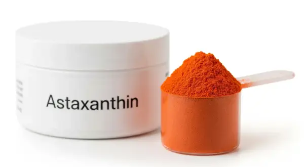 Biały pojemnik z napisem "Astaxanthin" obok miarki z pomarańczowym proszkiem. Czy astaksantyna skutki uboczne są groźne?