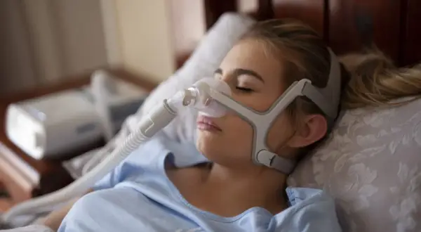 Kobieta śpi z maską CPAP, która pomaga w leczeniu bezdechu sennego. To jedno z domowych sposobów na spokojny sen.