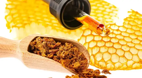 Propolis co to? Złocisty płyn z pipety i grudki propolisu na drewnianej łyżce na tle plastrów miodu.