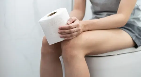 Kobieta siedzi na toalecie z rolką papieru. Czy witamina D3 a zapach moczu mogą być powiązane?