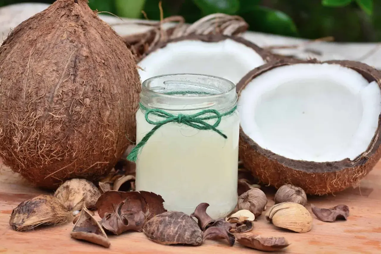 Słoik z olejem kokosowym, otoczony łupinami i połówkami kokosa. Wiele możliwości zastosowanie tego naturalnego produktu.
