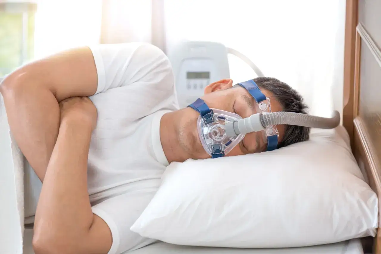 Mężczyzna śpi z maską CPAP, która pomaga w bezdechu sennym. To jedno z domowych sposobów na spokojny sen.