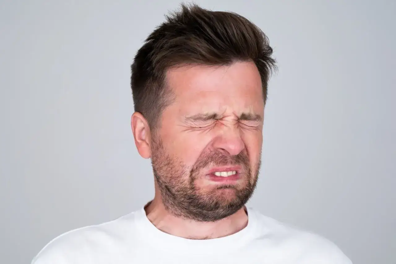 Mężczyzna z zamkniętymi oczami i skrzywioną miną, jakby poczuł gorzki smak w ustach.
