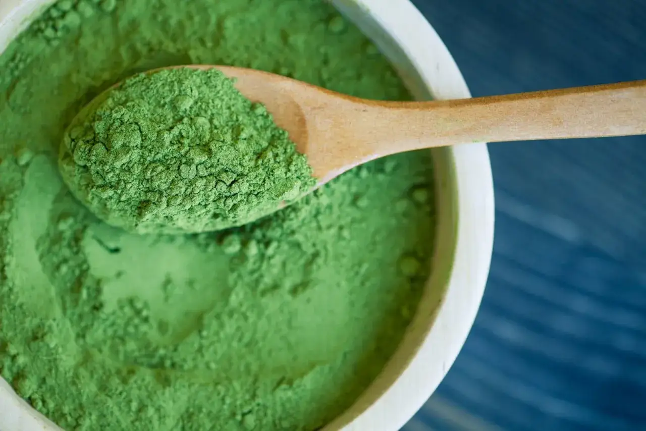 Zielony proszek na drewnianej łyżce i w misce. To spirulina, co to za superfood?