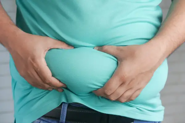 Osoba ściska brzuch, co może sugerować problemy zdrowotne, np. co podnosi trójglicerydy.