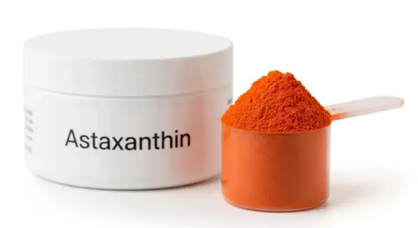 Biały pojemnik z napisem "Astaxanthin" obok miarki z pomarańczowym proszkiem. Czy astaksantyna skutki uboczne są groźne?