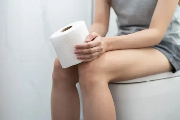 Kobieta siedzi na toalecie z rolką papieru. Czy witamina D3 a zapach moczu mogą być powiązane?
